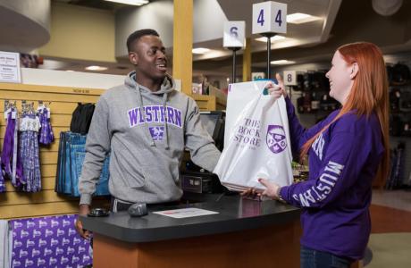 A western employee working in the bookstore hands a man a bag